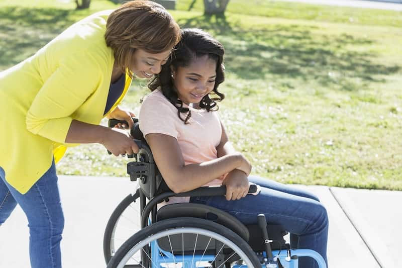 Child pushing a child in a wheelhair. They are happy.