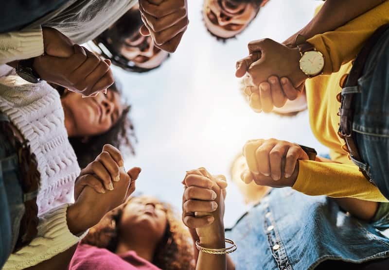 people holding hands in a circle where you only see the hands and the sun