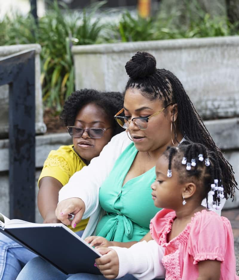 Black woman reading tow two young black children.